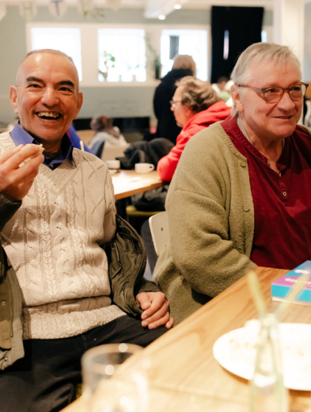 DünAmo Café: zwei Männer sitzen am Tisch, unterhalten sich und lächeln.