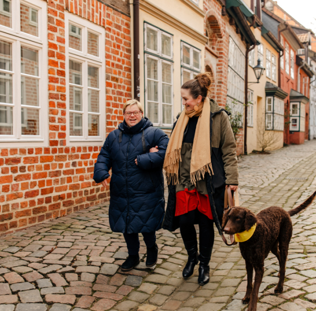 Zwei Frauen gehen mit einem braunen Hund spazieren.