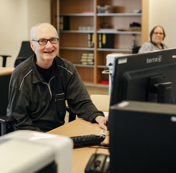 Ein Mann sitzt in einem Büro an einem Schreibtisch vor einem Computer.