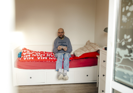 Ein Mann sitzt auf seinem Bett in seinem Zimmer.