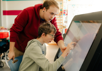 Ein Mann hilft einem Jungen mit Behinderung an einem großen Tablet.